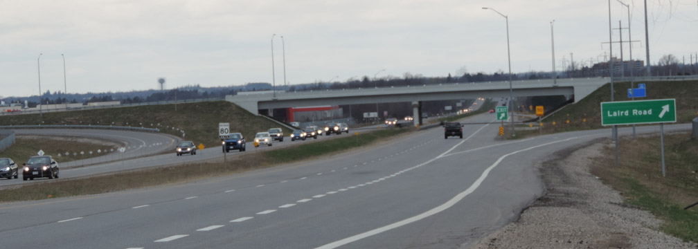 slide2 Highway with multiple lanes and vehicles in both directions, an overpass in the background, and a green sign for Laird Road.